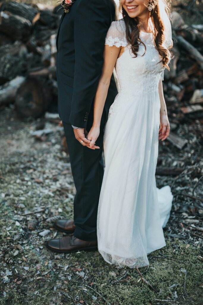 A wedding couple standing back to back with their hands linked.