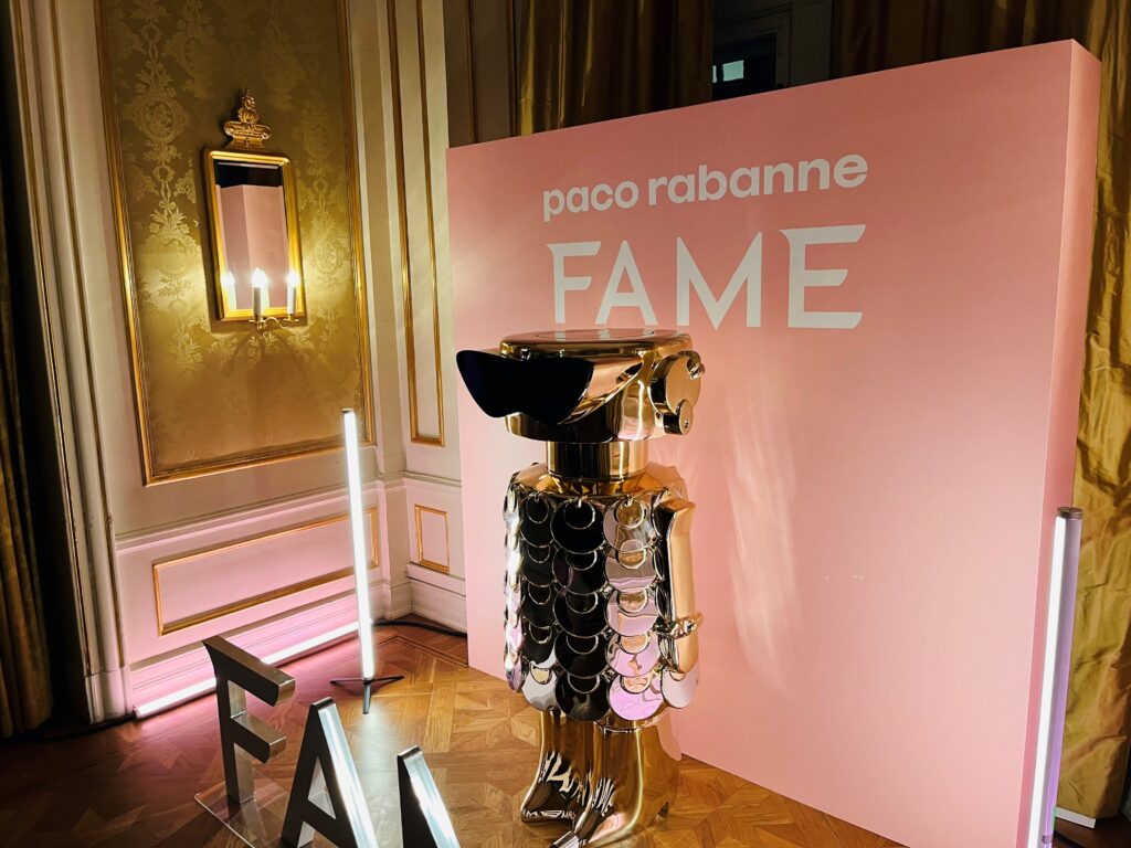 FAME doftdocka framför en rosa bakgrund med "paco rabanne FAME"-loggan på.